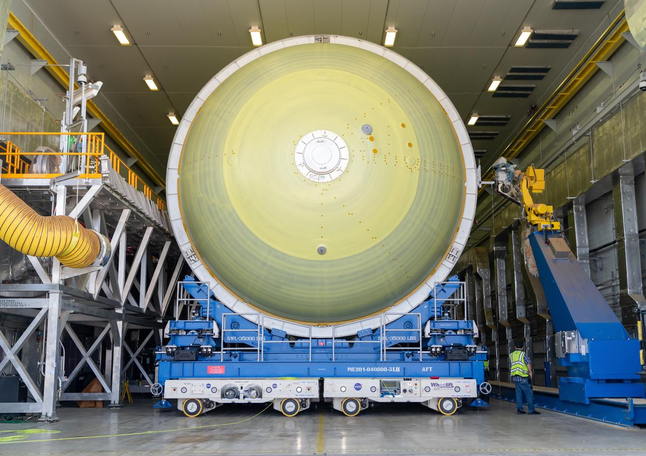 Teams move a liquid hydrogen tank for NASA’s SLS (Space Launch System) rocket out of a priming cell and into an adjacent cell on May 20 at the agency’s Michoud Assembly Facility in New Orleans. Inside the cell, the tank, which will be used on the core stage of NASA’s Artemis III mission, will receive its thermal protection system.  The thermal protection system, or spray-on foam insulation, provides protection to the core stage during launch. It is flexible enough to move with the rocket yet can withstand the aerodynamic pressures as the SLS accelerates from 0 to 17,500 mph and soars to more than 100 miles above the Earth. This third-generation insulation is more environmentally friendly and keeps the cryogenic propellant, which powers the rocket’s four RS-25 engines, extremely cold (the liquid hydrogen must remain at minus 423 degrees Fahrenheit/253 degrees Celsius) to remain in its liquid state. When applied the thermal protection system is a light-yellow color, which “tans” once exposed to the Sun’s ultraviolet rays, giving the SLS core stage its signature orange color.